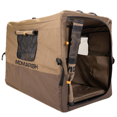 The MOmarsh Quick Crate by MOmarsh Inc. is a portable, soft-sided brown dog crate with mesh ventilation, a rolled-up front door for easy access, and is shown against a white background.